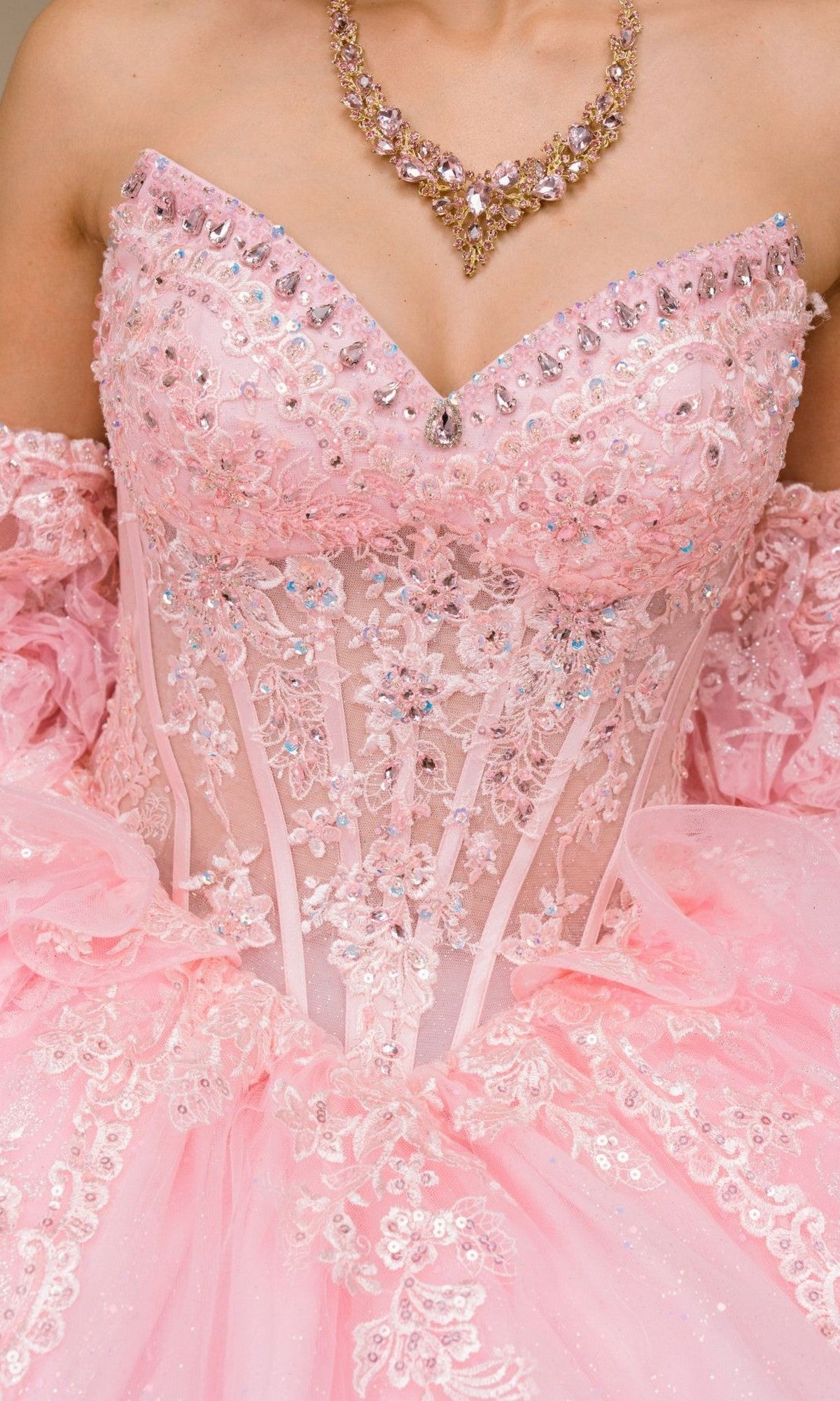 Person wearing the Quinceanera Dress 8535JQ by Cinderella Couture, an ornate strapless pink gown adorned with floral lace, rhinestones, and a matching jeweled necklace reminiscent of a classic quinceanera ball gown.
